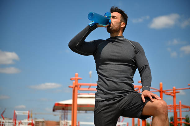 istock Muscular build handsome middle aged sportsman drinking water while resting after workout on the background of athletic field 1331239478