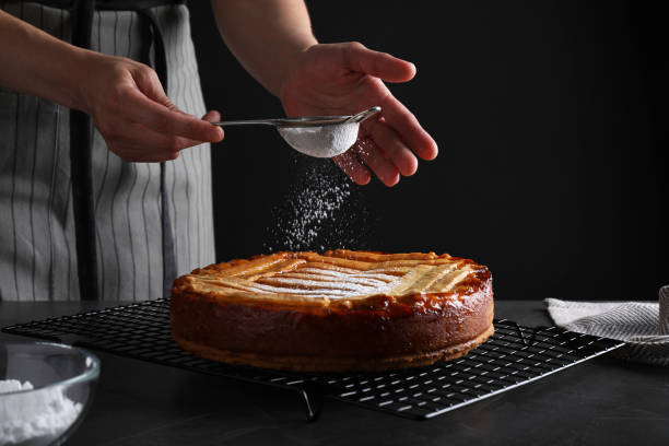 mujer decorando sabroso pastel de albaricoque con azúcar en polvo en la mesa negra, primer plano - cake women confectioner photography fotografías e imágenes de stock