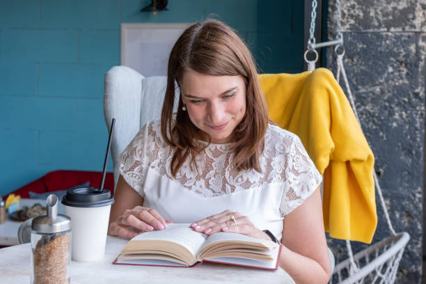 istock Beautiful smiling woman is drinking coffee and reading a book while sitting in a cafe. Reading paper books 1331243175