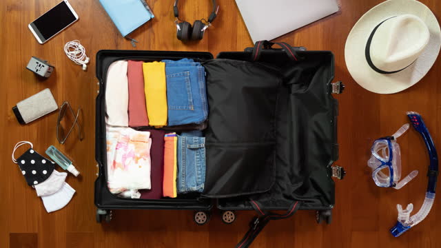 Stop-motion animation - packing bright yellow suitcase with face masks and sanitizer for summer holidays on wooden floor. Stuff quickly filling suitcase for new normal summer holidays concept.