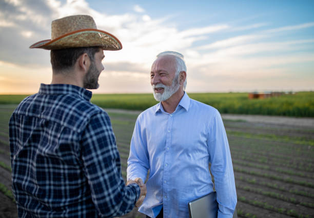 Farmer and insurance agent shaking hands in agricultural field in spring stock photo