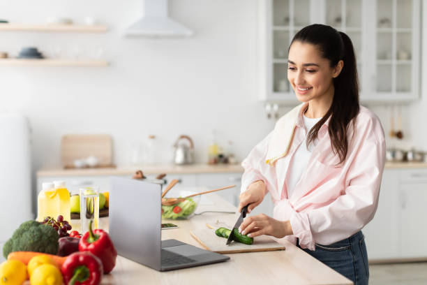 istock Woman cooking salad and using personal computer at kitchen 1331245457