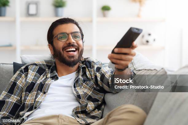 Relaxed Arab Guy Wathcing Movie On Tv Stock Photo - Download Image Now - Remote Control, Indian Ethnicity, Television Industry