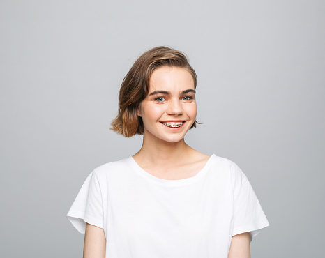 Portrait of beautiful young woman wearing white t-shirt. Female student smiling at camera. Studio shot, grey background.