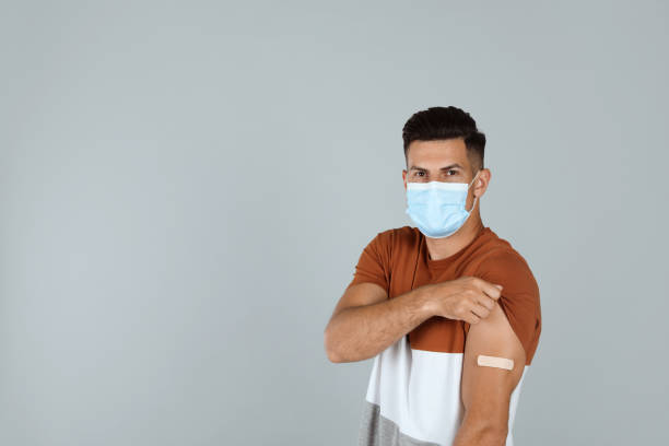 istock Vaccinated man with protective mask showing medical plaster on his arm against grey background. Space for text 1331249193