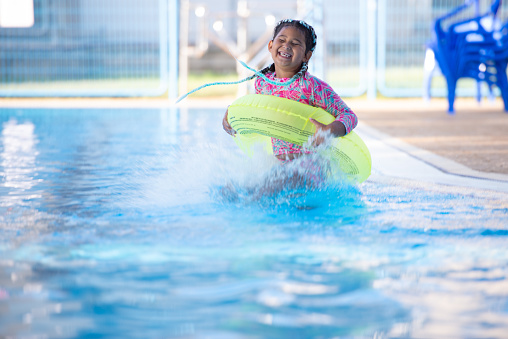 Girl jumping with the inflatable ring into the swimming pool.