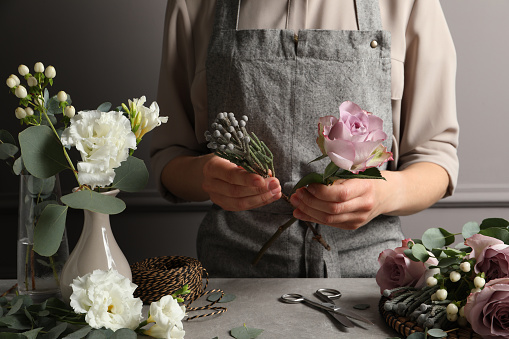 Florist creating beautiful bouquet at grey table, closeup