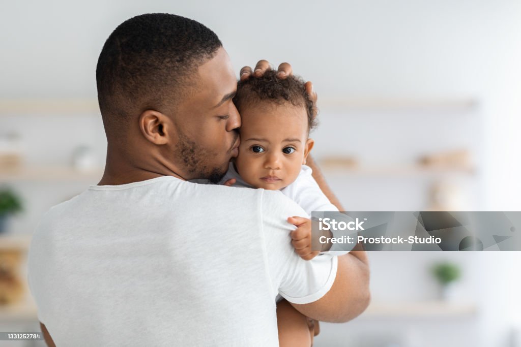 Father's Care. Young Black Dad Holding And Kissing Adorable Newborn Baby Father's Care. Young Black Dad Holding And Kissing Adorable Newborn Baby At Home, Cute Infant Child Looking At Camera, African American Daddy Bonding With His Son Or Daughter At Home, Closeup Shot Father Stock Photo