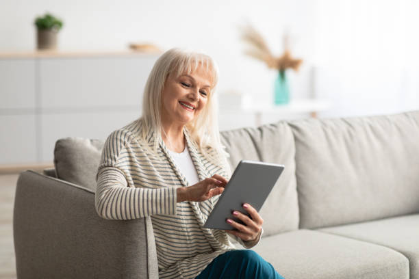 istock Smiling mature woman using tablet sitting on comfy couch 1331252948