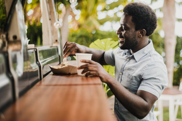 Young african man eating in food truck counter outdoor in city park - Focus on face Young african man eating in food truck counter outdoor in city park - Focus on face black people bar stock pictures, royalty-free photos & images