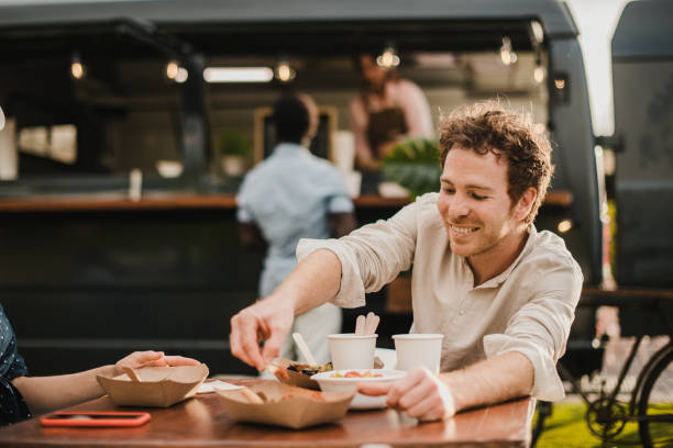 jovens felizes comendo em food truck ao ar livre - foco no rosto do homem - street food - fotografias e filmes do acervo