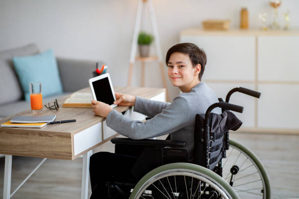 istock Positive disabled teenager in wheelchair using tablet computer, having online lesson or webinar at home 1331254839