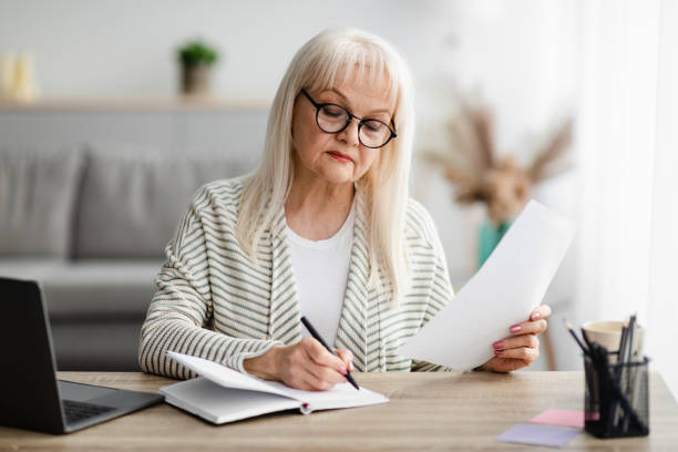 istock Focused mature woman writing and holding document at home 1331255886