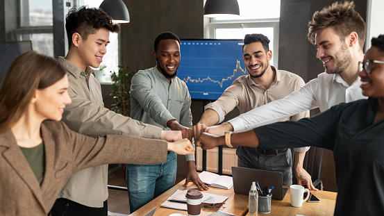 Success And Connection Concept. Smiling multiracial group of diverse business people making fist bump standing in circle. Happy colleagues pumping hands together as symbol of unity and achievement
