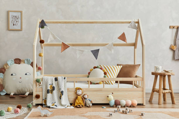 istock Creative composition of cozy scandinavian child's room interior with mock up poster frame, balance board, plush and wooden toys and hanging decorations. Neutral wall, carpet on the floor. Template. 1331256046