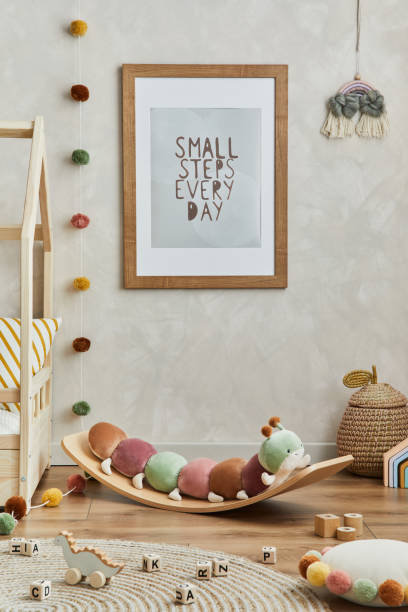 istock Creative composition of cozy scandinavian child's room interior with mock up poster frame, balance board, plush and wooden toys and hanging decorations. Neutral wall, carpet on the floor. Template. 1331256078