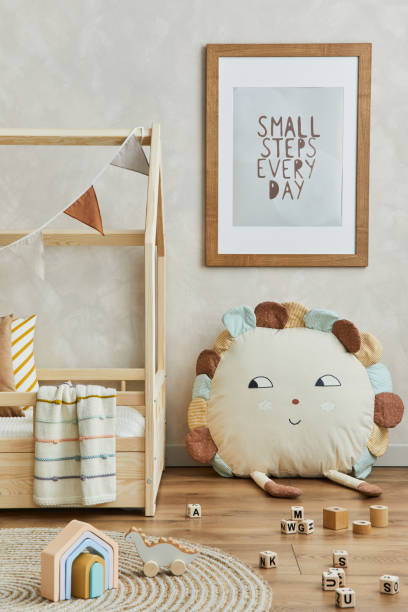 istock Creative composition of cozy scandinavian child's room interior with mock up poster frame, balance board, plush and wooden toys and hanging decorations. Neutral wall, carpet on the floor. Template. 1331256080