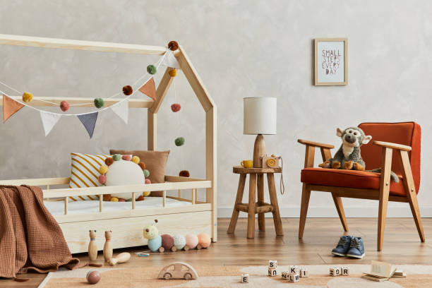 istock Creative composition of cozy scandinavian child's room interior with mock up poster frame, balance board, plush and wooden toys and hanging decorations. Neutral wall, carpet on the floor. Template. 1331256100