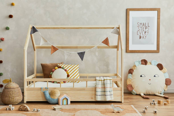 istock Creative composition of cozy scandinavian child's room interior with mock up poster frame, balance board, plush and wooden toys and hanging decorations. Neutral wall, carpet on the floor. Template. 1331256123