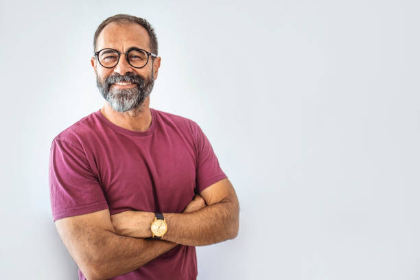 Portrait of happy mature man wearing spectacles and looking at camera indoor. Portrait of happy mature man wearing spectacles and looking at camera indoor. Man with beard and glasses feeling confident.  Handsome mature man posing against a grey background 45 49 years stock pictures, royalty-free photos & images