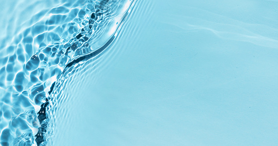 Defocused blue liquid water waves in sunlight background. Trendy summer nature banner
