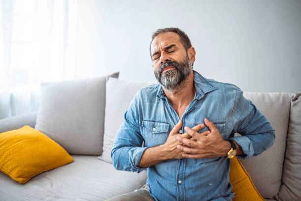 Closeup shot of a mature man holding his chest in discomfort at home. Closeup shot of a mature man holding his chest in discomfort at home. Shot of a handsome mature businessman holding his chest in pain while relaxing on a sofa at home male chest pain stock pictures, royalty-free photos & images