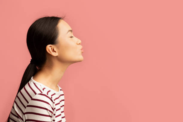 Side View Portrait Of Young Asian Woman Sending Air Kiss Side View Portrait Of Young Asian Woman Sending Air Kiss, Profile Shot Of Attractive Millennial Korean Lady Pouting Lips While Standing Isolated Over Pink Background, Panorama With Copy Space puckering stock pictures, royalty-free photos & images