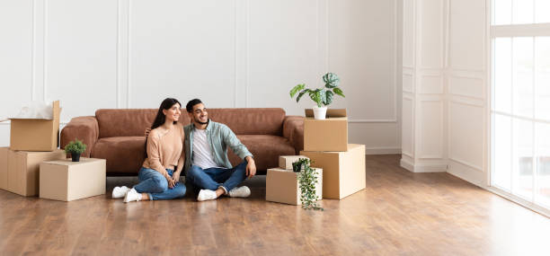 Family relaxing on floor in new home with cardboard boxes Moving Day. Lovely couple sitting on the floor in new home with cardboard boxes around. Happy man and woman dreaming, looking aside at window, free copy space, panoramic banner for advertisement moving house stock pictures, royalty-free photos & images