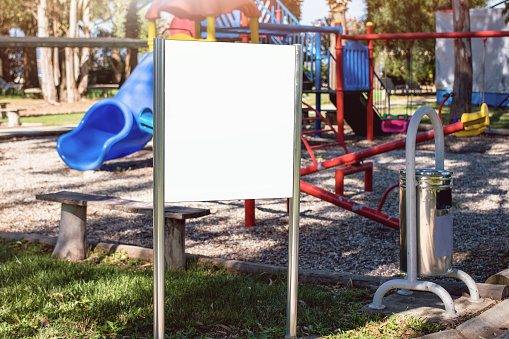 White empty poster with mockup place stands on children playground at summer day outdoor