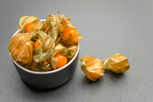 Physalis fruits against black background. Sweet yellow physalis berries in a cup on a dark table top, place to insert text or design.