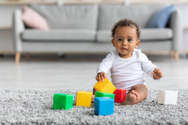 adorable black infant baby playing with stacking building blocks at home - baby stockfoto's en -beelden