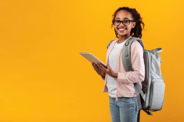 istock Black girl standing with tablet at yellow studio wall 1331261937