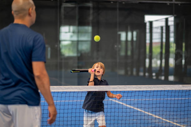 surveiller l’enseignement de la classe de padel à l’enfant, son élève - l’entraîneur enseigne au petit garçon comment jouer au padel sur un court de tennis intérieur - indoor tennis photos photos et images de collection