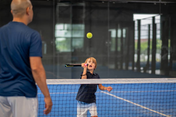 Monitor teaching padel class to child, his student - Trainer teaches little boy how to play padel on indoor tennis court Monitor teaching padel class to child, his student - Trainer teaches little boy how to play padel on indoor tennis court tennis coach stock pictures, royalty-free photos & images