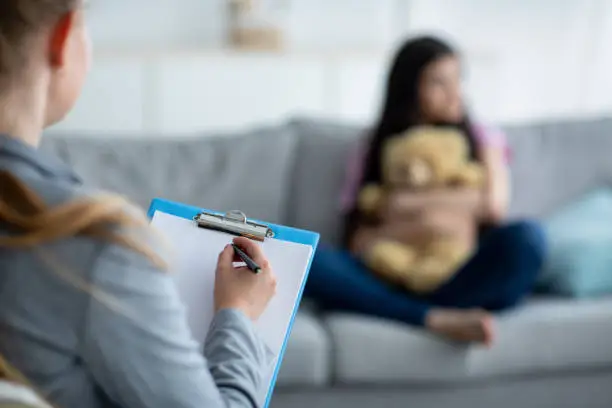 Teenage depression. Psychologist working with upset teen girl at office, talking to her patient, taking notes, selective focus. Unhappy adolescent having consultation with psychotherapist, copy space