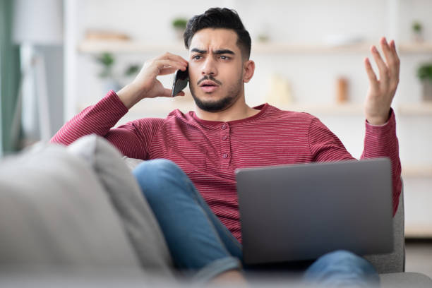istock Angry man with notebook on his lap having phone conversation 1331265196