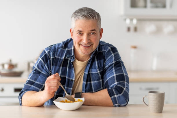 istock Healthy breakfast concept. Cheerful senior man having breakfast, eating cereals and drinking coffee, free space 1331266773