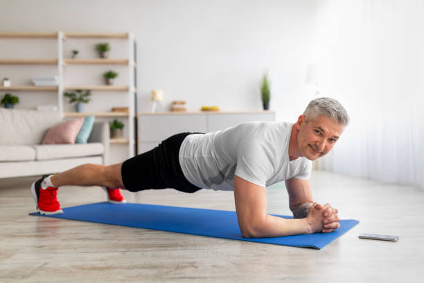 sport et perte de poids à la maison. homme mature sportif debout dans la planche du coude, renforçant ses muscles du tronc, espace libre - core strength photos et images de collection