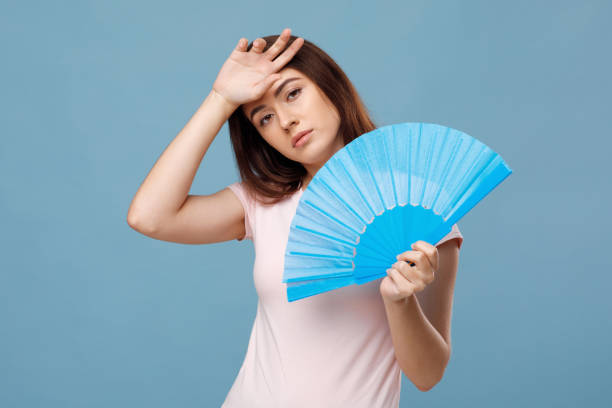 istock Tired young lady with fan touching her sweaty head 1331267904