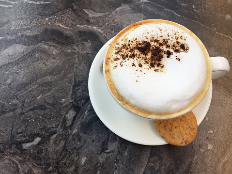 Frothy drink cappuccino on the marble coffee table with cookie