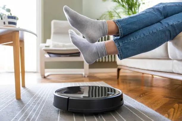 Young woman lift up the feet for letting robotic vacuum cleaner pass though