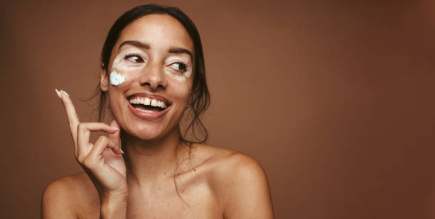Melanin skin care routine Smiling woman applying facial mask. Close up of young woman applying product for skincare. imperfection stock pictures, royalty-free photos & images