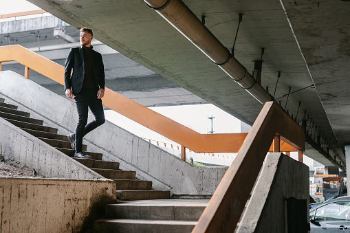 Handsome young businessman walking down the bridge stairs while looking away