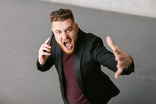 Young redhead furiously arguing on the phone while looking at camera