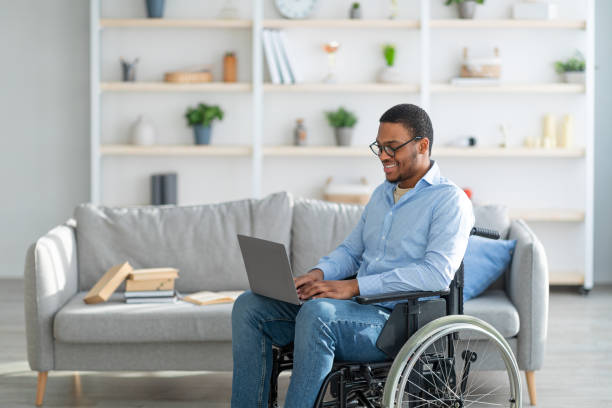 istock Cheerful handicapped black guy in wheelchair using laptop for work or studies, having remote job at home, copy space 1331274108