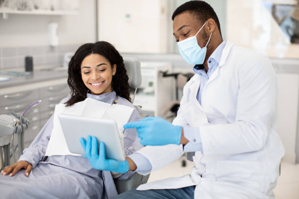 black dentist doctor with digital tablet consulting female patient in modern clinic - dentist surgery dental hygiene using voice imagens e fotografias de stock