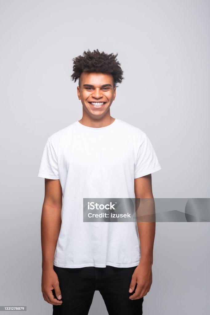 Friendly young man in white t-shirt Portrait of cheerful young man wearing white t-shirt. Male student smiling at camera. Studio shot, grey background. T-Shirt Stock Photo