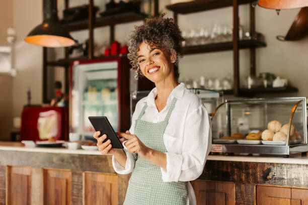 lächelnde unternehmerin mit einem digitalen tablet in ihrem café - barista fotos stock-fotos und bilder
