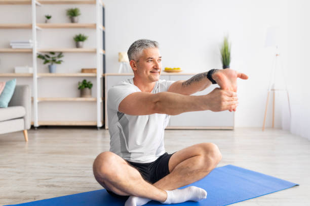 istock Morning workout at home. Mature man doing stretching for hand exercises, training at home, sitting on mat, free space 1331281353