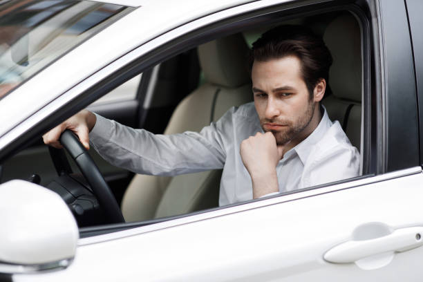 Traffic jam in city, negative emotions, road to work. Sad unhappy tired caucasian handsome male businessman in suit driving in cabin and pondering during stop, looks at open window, free space